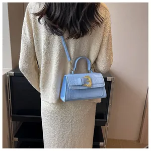 Blue crocodile pattern crossbody bag with a large golden buckle worn by a model
