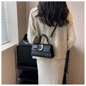 Detail of black crocodile embossed shoulder bag with golden baroque buckle on a model