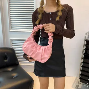 Pink ruched croissant bag with half-moon shape held by a model in casual outfit