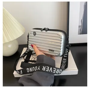 Detailed view of silver suitcase-style crossbody bag with Forever Young metal logo