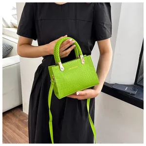 Detail of bright green crocodile-embossed leather handbag with woven handle and gold hardware