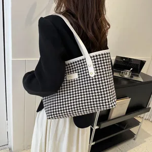 Detail of large houndstooth tote bag with white leather straps and gold logo plate