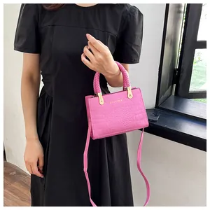 Detail of a bright pink crocodile pattern crossbody bag with a woven handle and gold hardware