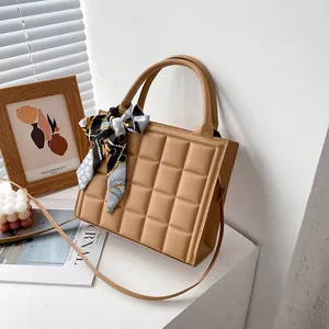Quilted khaki crossbody bag with silk scarf handle on minimalist artistic background
