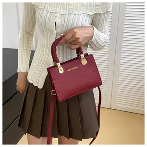 Detail of burgundy crocodile pattern handbag with metallic handles held by model