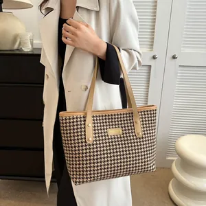 Detail of brown houndstooth tote bag with leather straps and metal brand plate