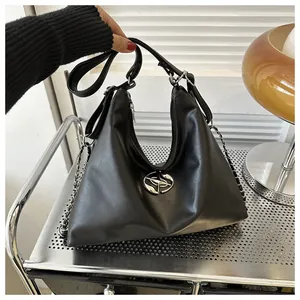 Detail of black trapezoid leather bag showing silver logo and chain strap on a desk