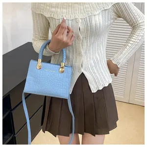Close-up of light blue crocodile embossed handbag with woven handle and gold hardware