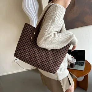 Close-up of brown houndstooth tote bag with leather straps and gold metal rivets
