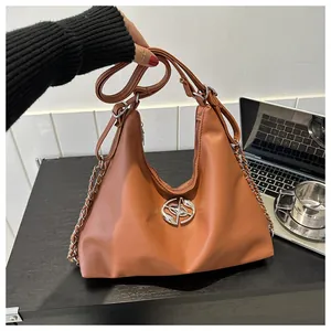 Detailed close-up of brown PU leather bag with silver circular logo and chain ornament