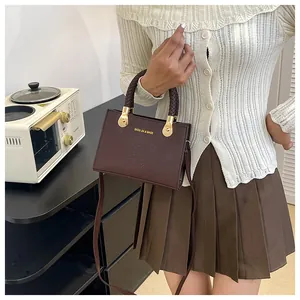 Detail of brown crocodile pattern handbag with woven handle and metallic accents