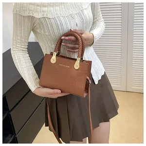 Close-up of brown crocodile pattern square bag featuring a braided handle and gold hardware
