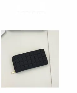 Detail of black long wallet featuring square embossed pattern and gold zipper closure