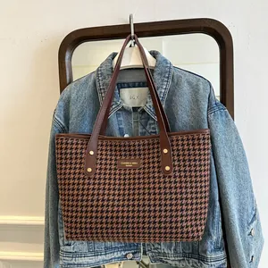 Detail of houndstooth tote bag with leather straps and metal logo on denim jacket