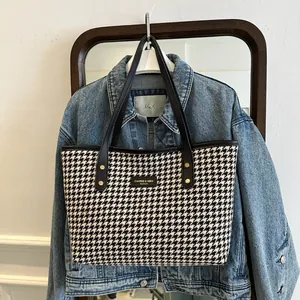 Detail of classic houndstooth tote bag featuring leather handles and gold metal rivets