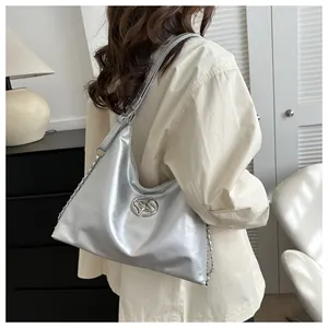 Detail of silver metallic underarm bag with circular metal logo and chain strap