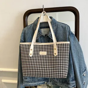 Detail view of large houndstooth tote bag with white leather straps and golden rivets