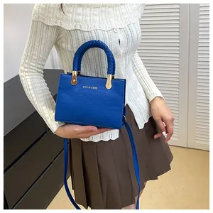 Detail of royal blue crocodile pattern handbag with woven handle and gold hardware