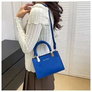 Detail of blue crocodile pattern handbag featuring a woven handle and gold lettering
