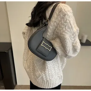 Detail of black crescent shoulder bag with gold metal buckle on a knitted sweater