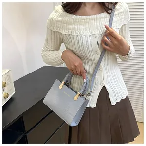 Detail of light blue crocodile pattern bag with braided handle and gold metal hardware