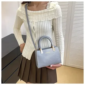 Detail of blue-grey crocodile embossed leather bag with a woven handle and gold hardware