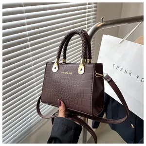 Detail of dark brown crocodile pattern leather handbag with woven handle and gold hardware