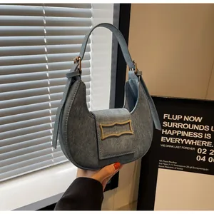 Detailed close-up of crescent denim shoulder bag with golden hardware and buckle strap