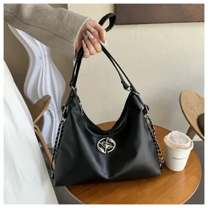 Detail of black PU leather hobo bag with silver logo and chain strap on a wooden table
