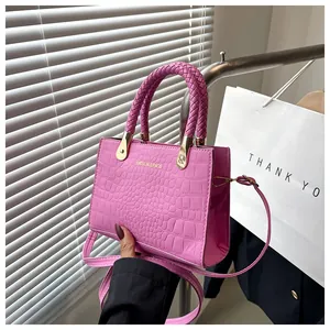 Pink crocodile-embossed handbag detail featuring woven handles and golden metal hardware
