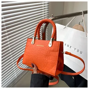 Detail of bright orange crocodile embossed leather handbag with woven handles and gold hardware