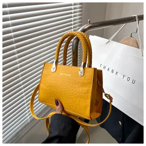 Detail of yellow crocodile embossed handbag with braided handles and gold hardware