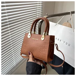 Detail of brown croc-embossed handbag with woven handle and metallic logo on PU leather