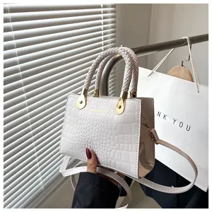 Detail of white crocodile texture handbag with woven handle and gold metal hardware