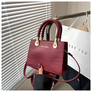 Detail of burgundy crocodile-embossed handbag with woven handle and gold-tone hardware