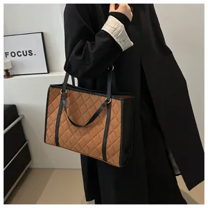 Macro view of large brown suede tote bag with diamond quilted pattern and black handles