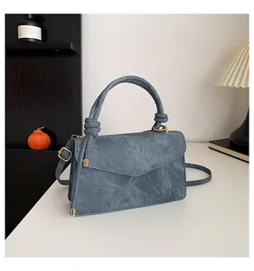Detail of blue denim texture crossbody bag with knotted handle and golden hardware