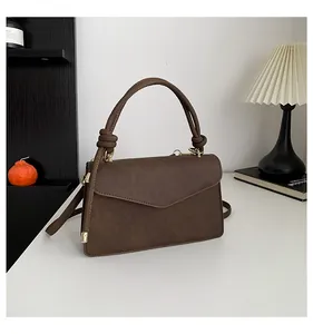 Detailed view of dark brown crossbody bag featuring knotted handle and gold metal hardware