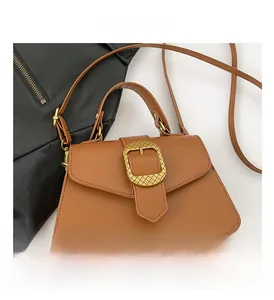 Detail view of brown trapezoid handbag featuring a textured gold buckle and top handle
