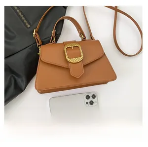 Macro detail of brown trapezoid bag featuring textured matte gold buckle and leather handle