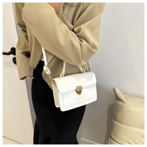 Detail view of white square bag with golden lock and adjustable strap on a model
