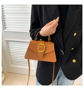 Close-up of brown leather bag with textured gold square buckle and detachable strap
