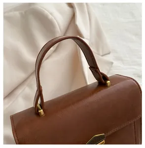 Detail of comfortable leather handle on a retro brown small square bag with gold hardware