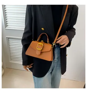Brown trapezoid leather handbag with gold woven buckle detail on black blazer outfit
