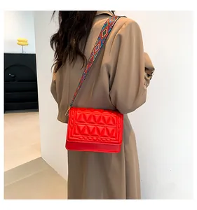 Detail of red quilted crossbody bag with stylish geometric pattern woven strap
