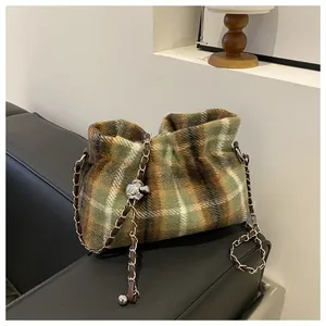 Detail of plaid wool bucket bag with woven chain strap on a black leather sofa