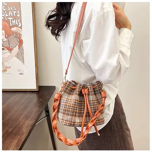 Woman wearing plaid woolen bucket bag with braided strap and orange-brown leather details