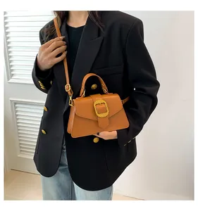 Detail of caramel leather handbag featuring a large textured gold buckle and top handle