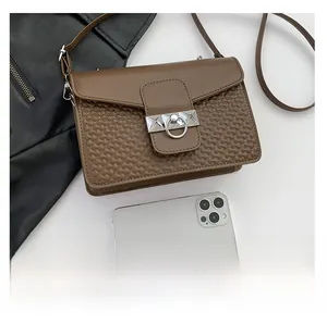 Detailed view of brown wavy embossed crossbody bag next to a smartphone for size reference