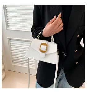 Detail of white leather crossbody bag with a large textured gold buckle and top handle